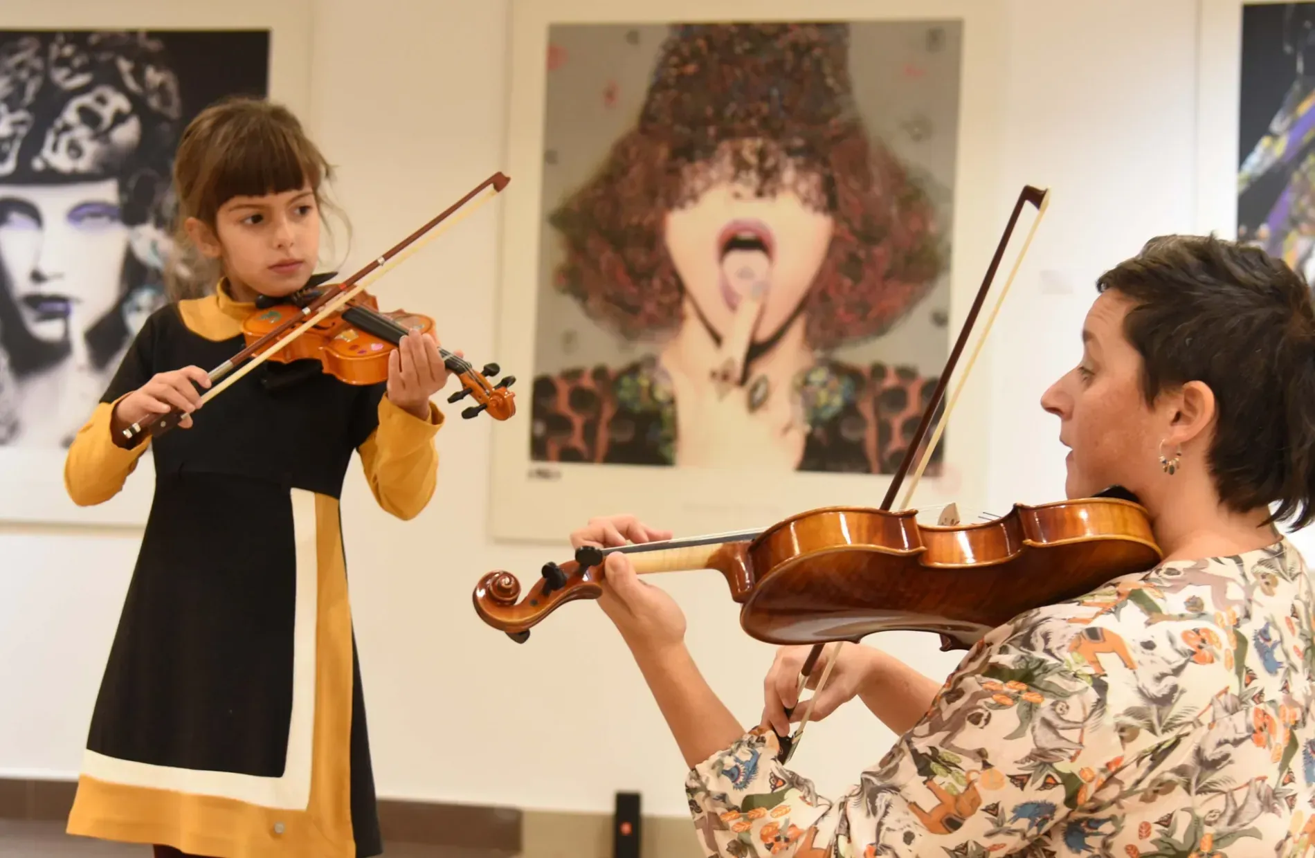 Una mujer le está enseñando a una niña a tocar el violín.