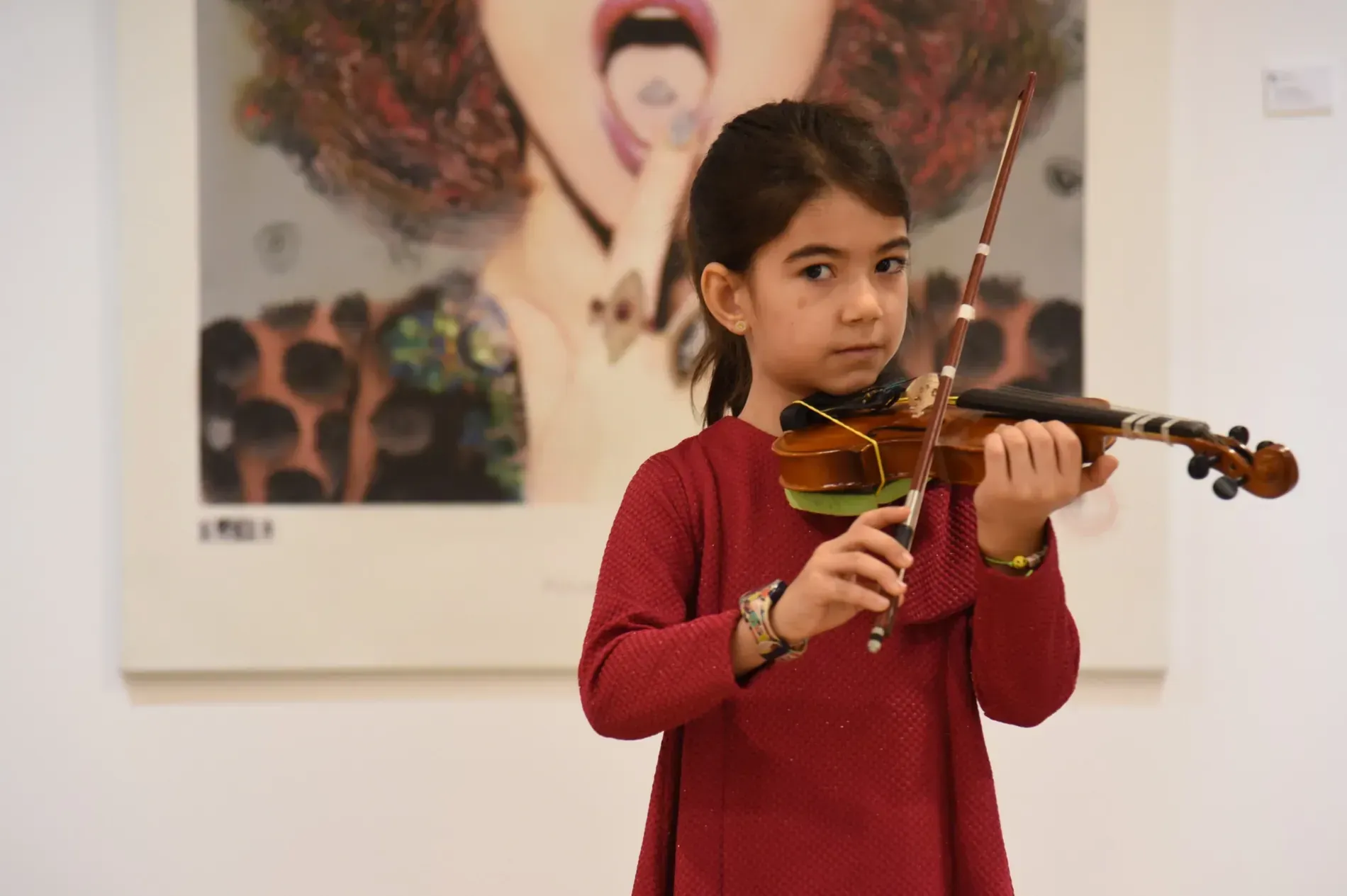 Una niña toca un violín delante de un cuadro de una mujer.
