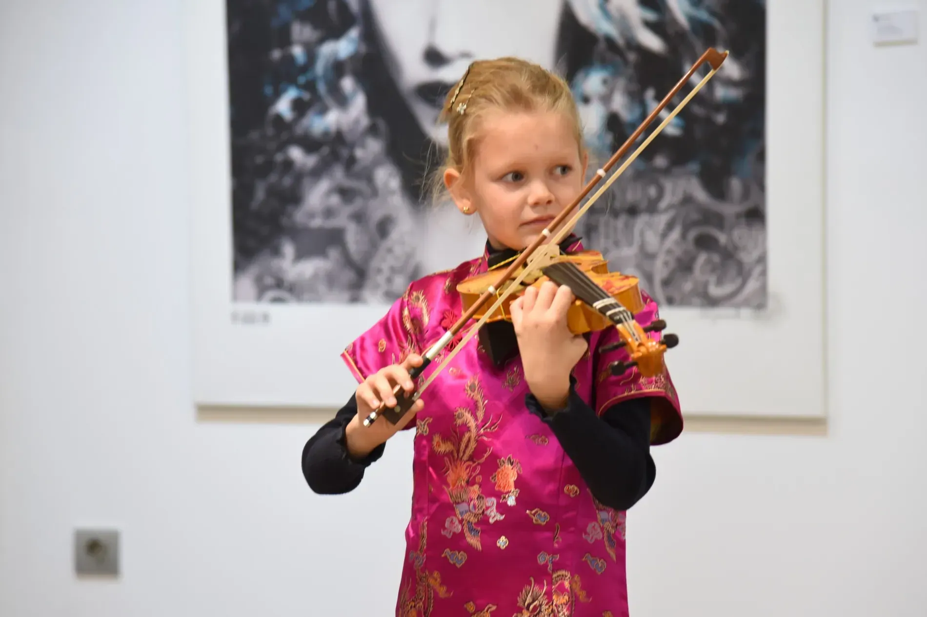 Una niña con un vestido rosa está tocando un violín.