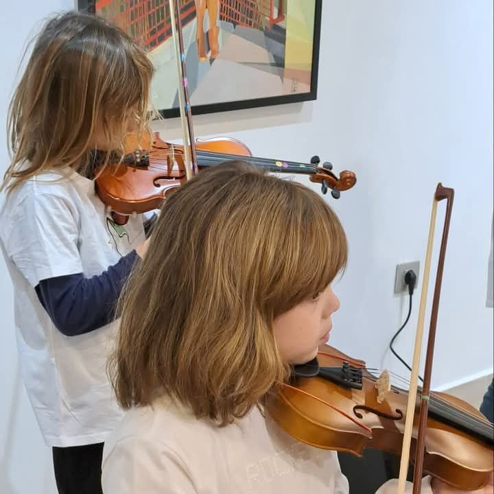 Dos chicas jóvenes están tocando violines en una habitación.