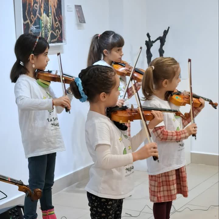 Un grupo de chicas jóvenes tocan violines en una habitación.