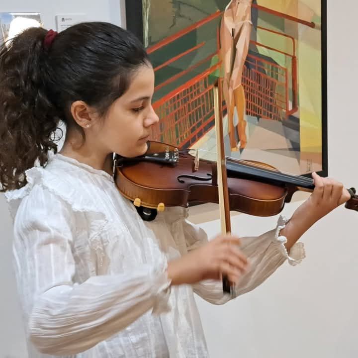 Una niña toca el violín delante de un cuadro.