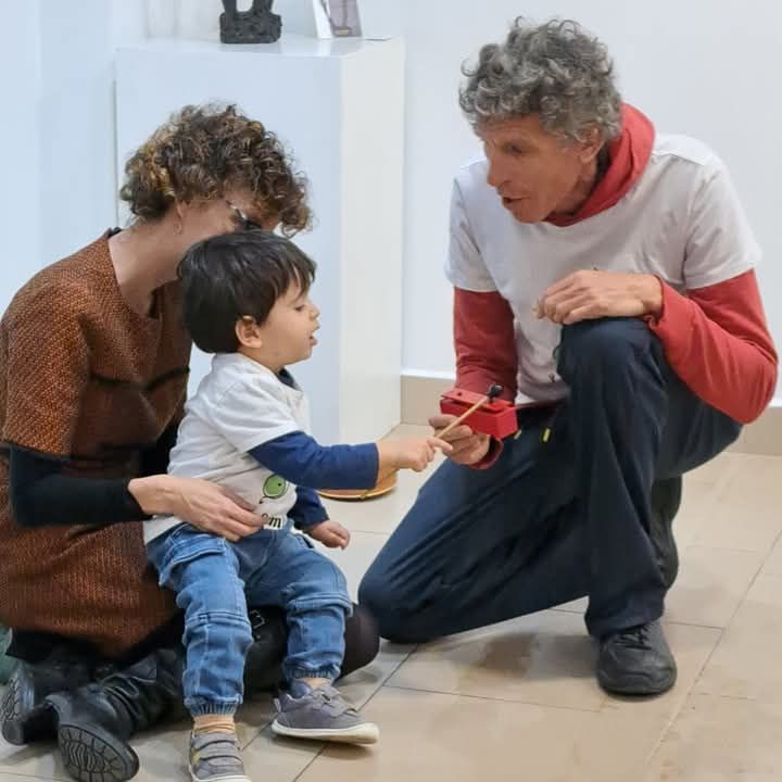 Un niño pequeño está sentado en el suelo con dos personas.
