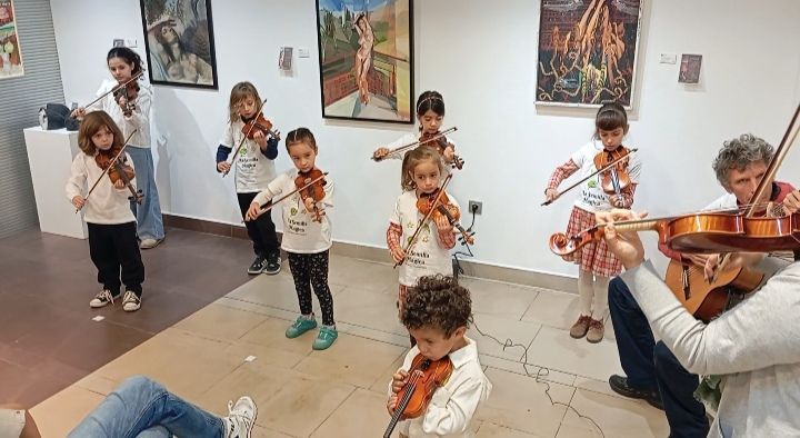 Un grupo de niños está tocando violines en una habitación.