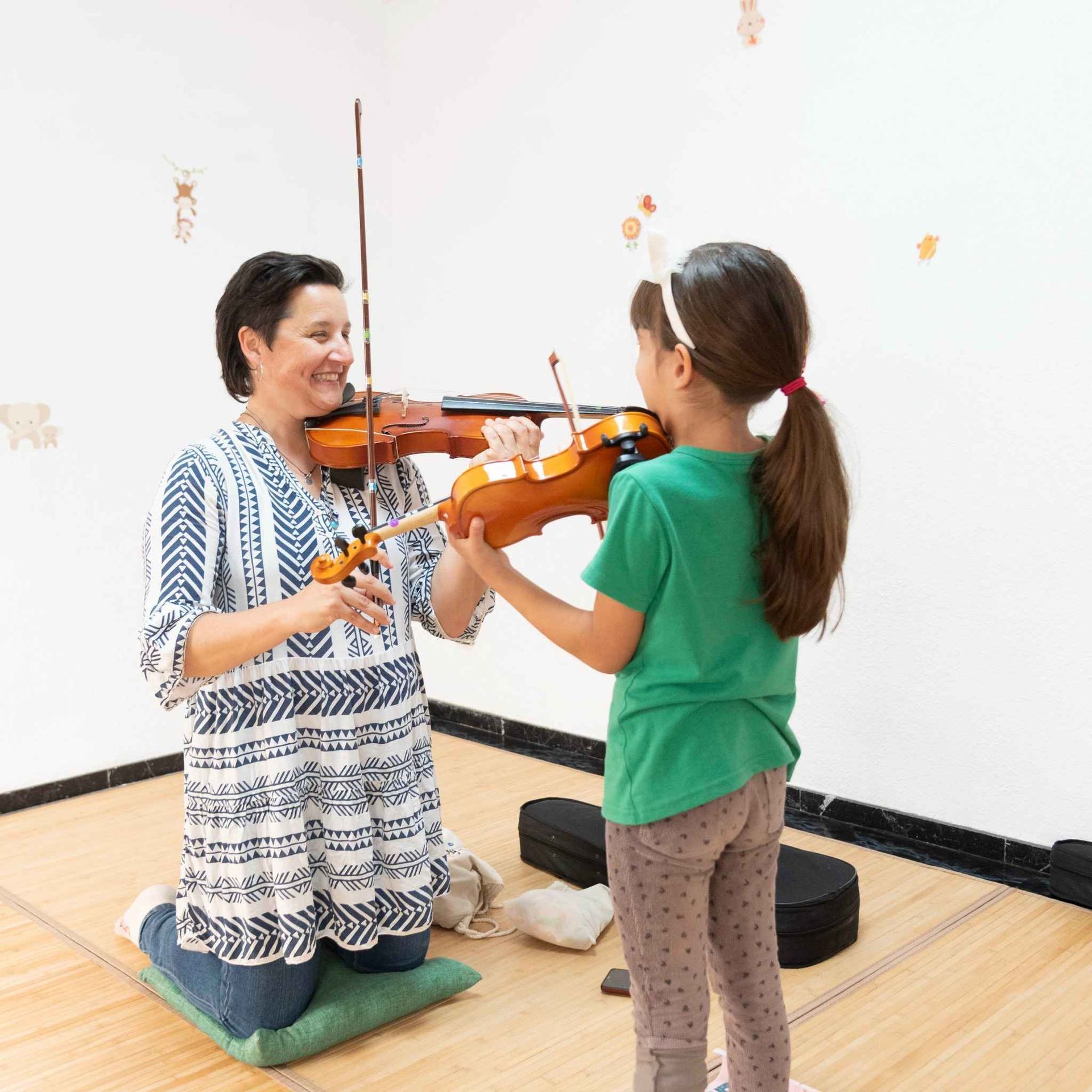 Una mujer le está enseñando a una niña a tocar el violín.