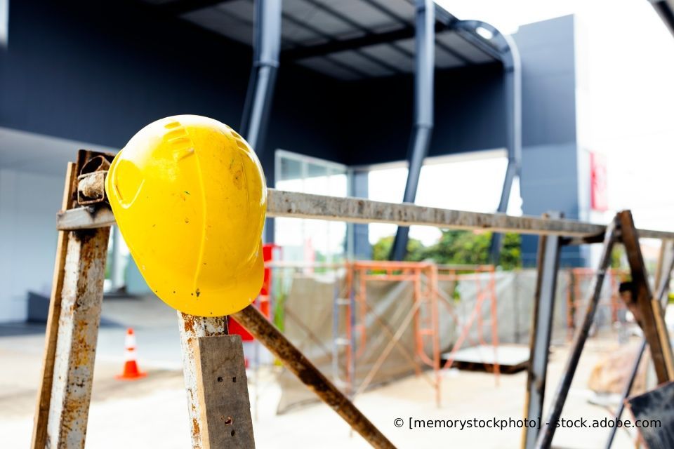 Gelber Schutzhelm auf einer Metallbarriere auf einer Baustelle.