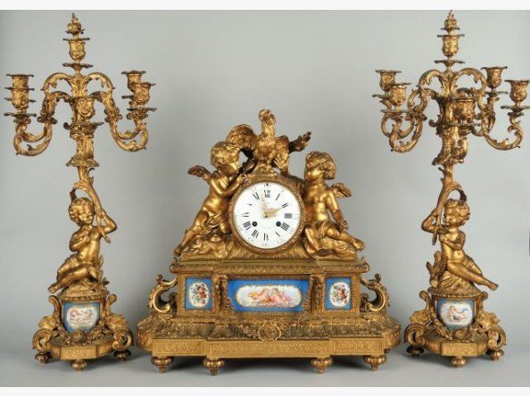 Pendule rococo dorée avec angelots, deux candélabres, cadran blanc, détails bleus et floraux.