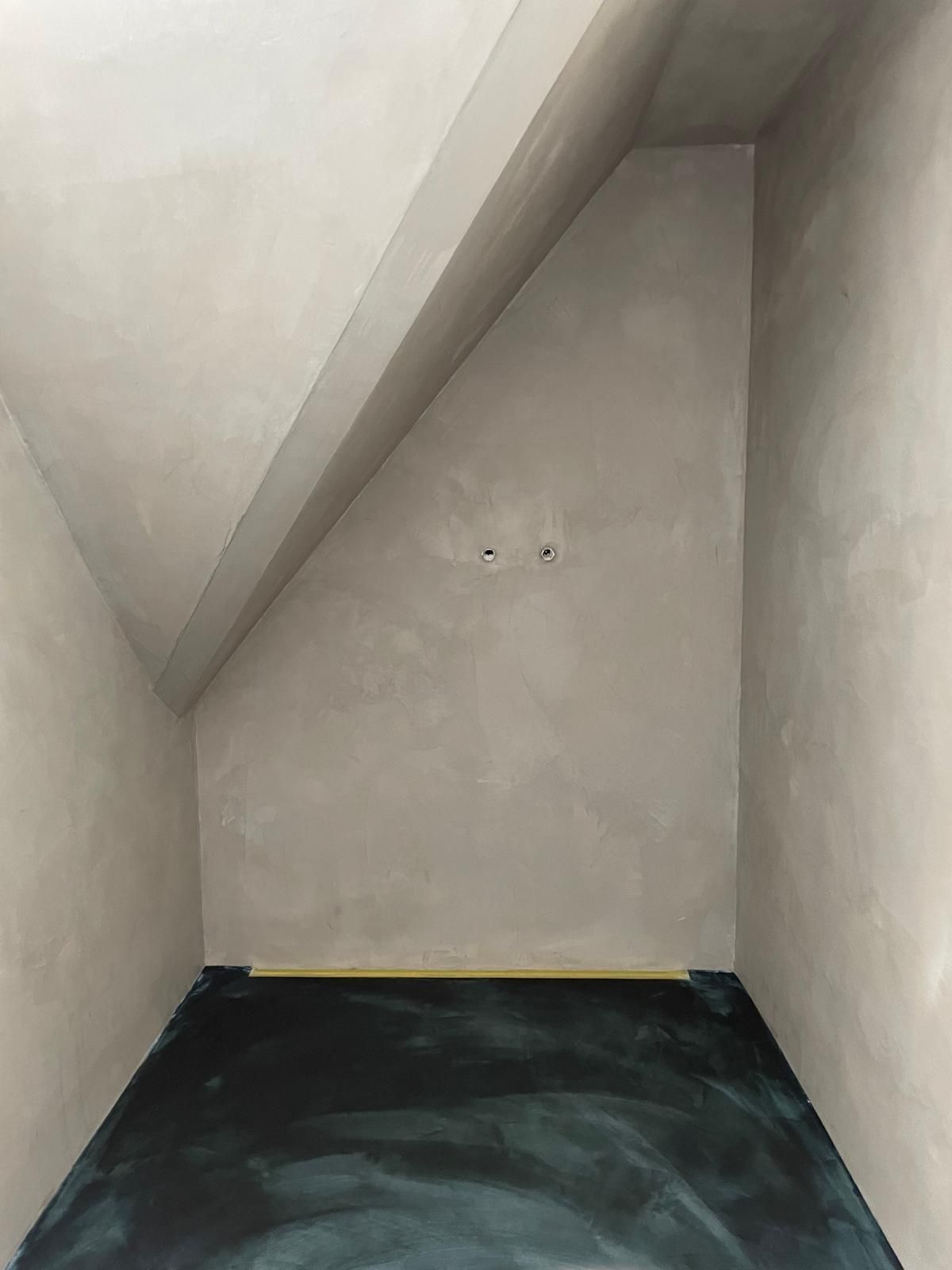 Ein sehr kleiner Raum mit schräger Decke und schwarzem Boden.