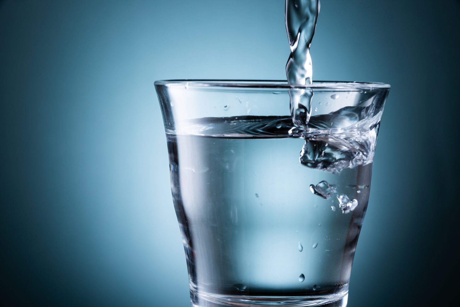De l'eau claire est versée dans un verre sur un fond bleu foncé.