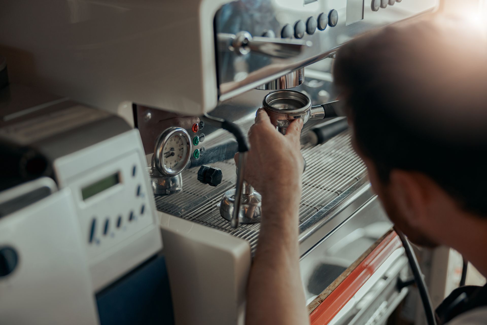 Une personne s'apprête à insérer un porte-filtre dans une machine à expresso professionnelle, dans un café.