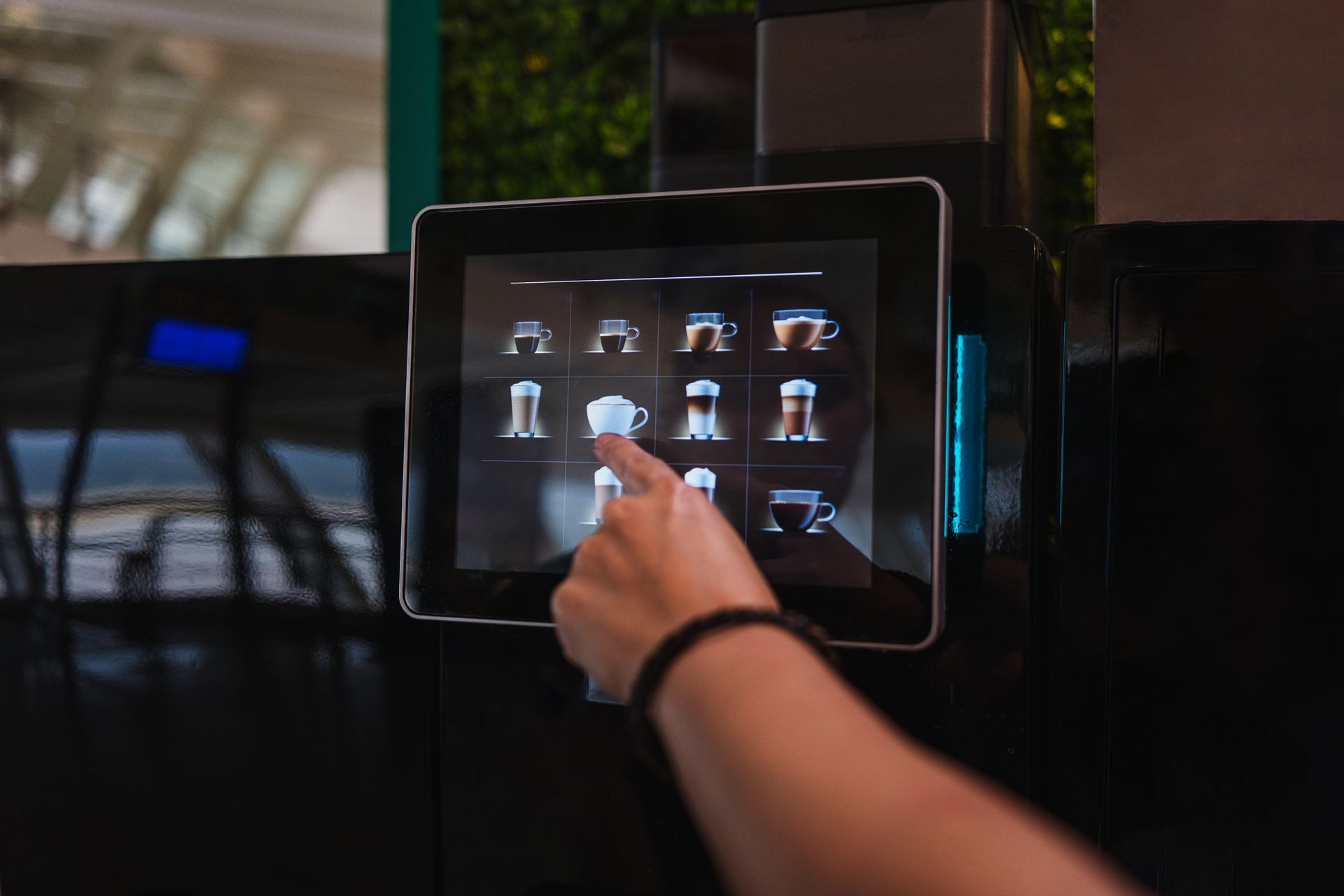 Une main effleure l'écran tactile d'une machine à café noire.