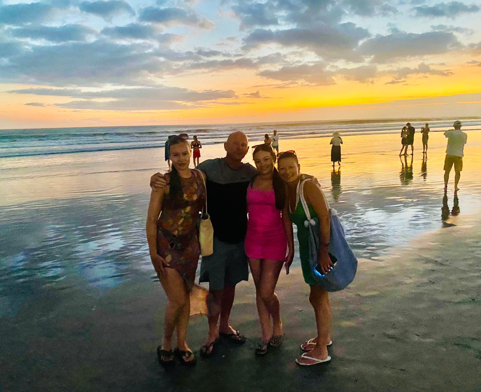 A group of people are posing for a picture on a beach at sunset.