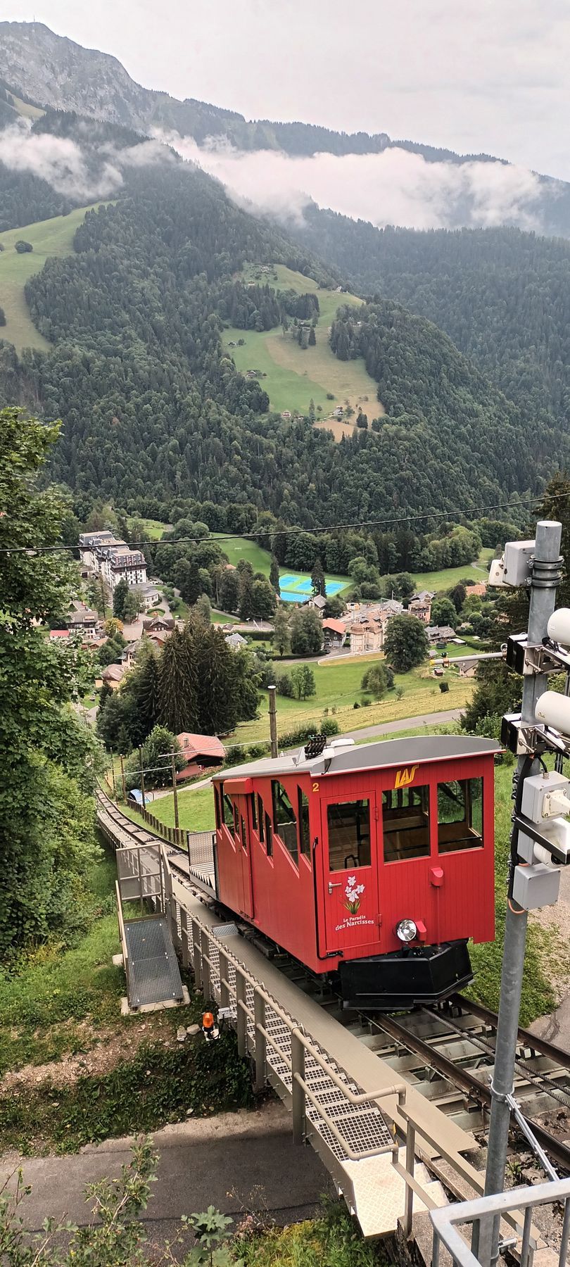 A red train is going down the tracks in the mountains.