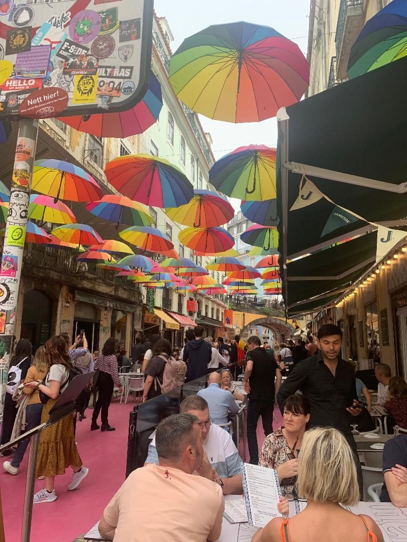 A group of people are sitting at tables under colorful umbrellas.