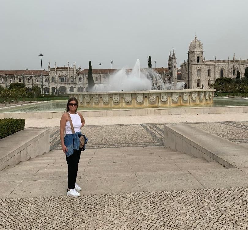 A woman is standing in front of a fountain in a park.