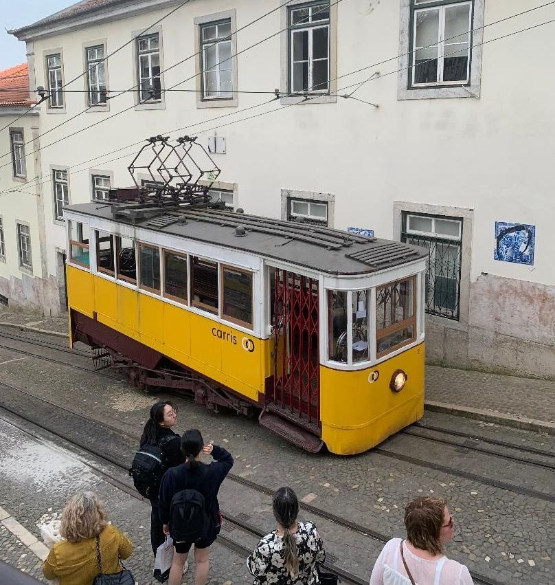 A yellow trolley is going down a hill in front of a building.