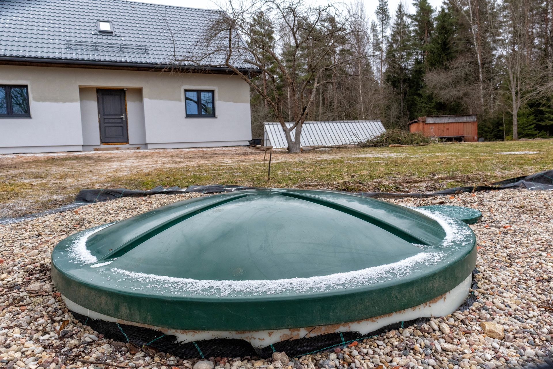 Réservoir souterrain vert en forme de dôme dans une cour gravillonnée à côté d'une maison et d'arbres