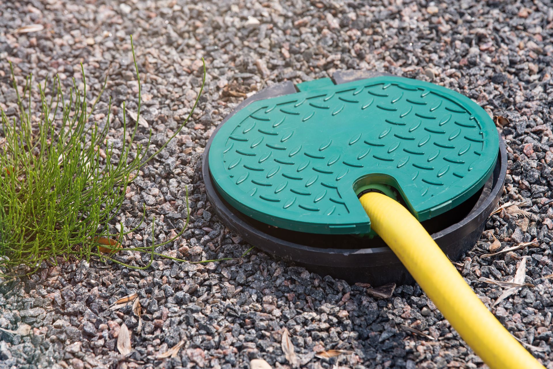 Tuyau jaune fixé à un couvercle utilitaire rond et vert sur du gravier