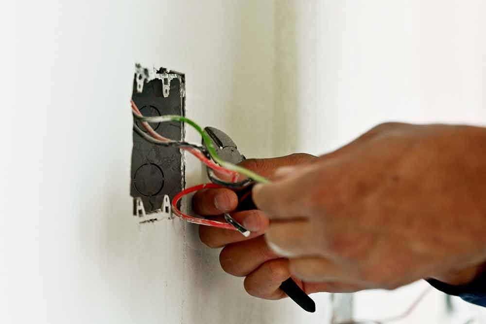 Eine Person arbeitet mit einer Zange an einer Steckdose.