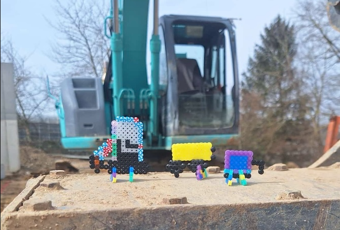 Ein Spielzeuglastwagen steht auf einem Erdhaufen neben einem Bagger.