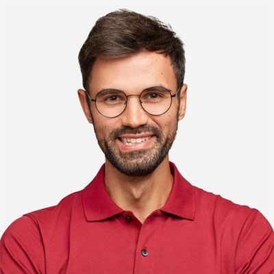 Un homme portant des lunettes et un polo rouge sourit.