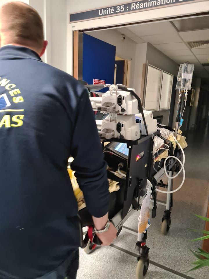 Ambulancier de dos des Ambulance Thomas poussant un brancard dans un couloir d'hôpital