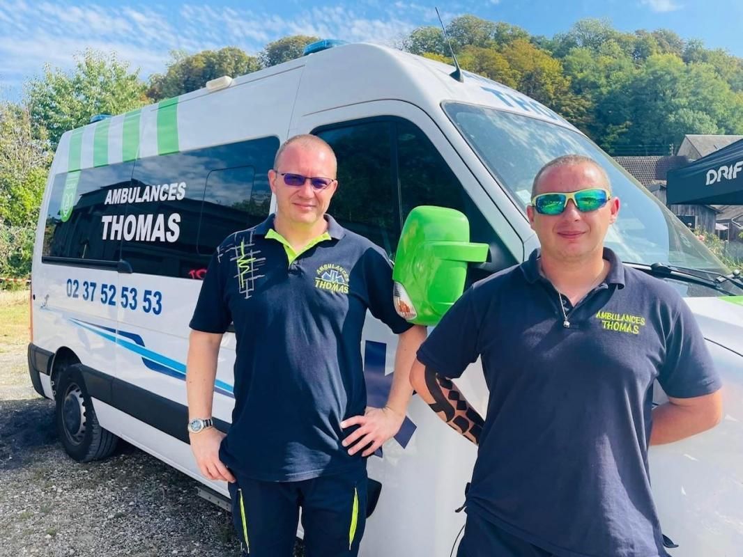 Deux hommes portant des lunettes de soleil posant devant un véhicule des Ambulances Thomas