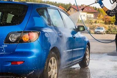 Eine Person wäscht ein blaues Auto mit einem Hochdruckreiniger.