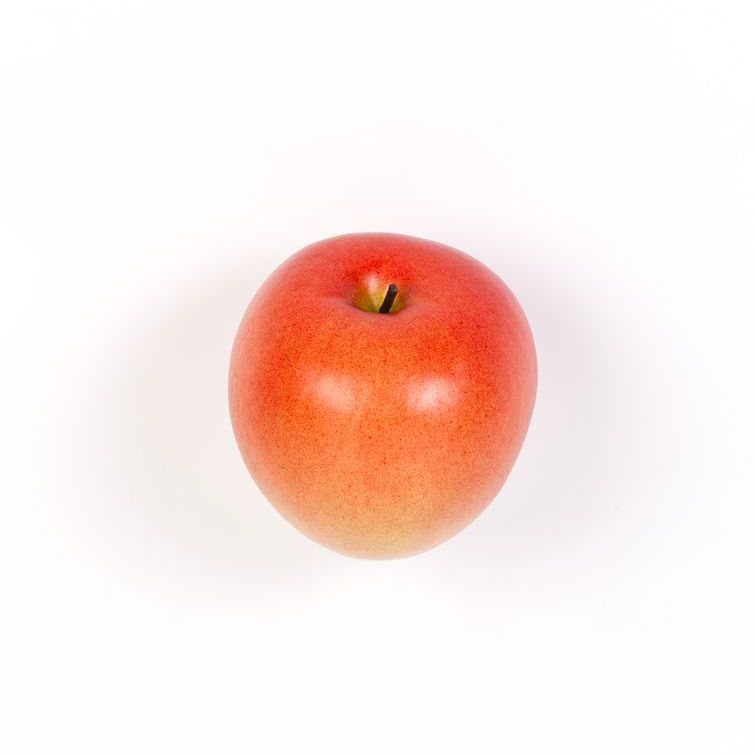 Una manzana roja está sobre una superficie blanca.