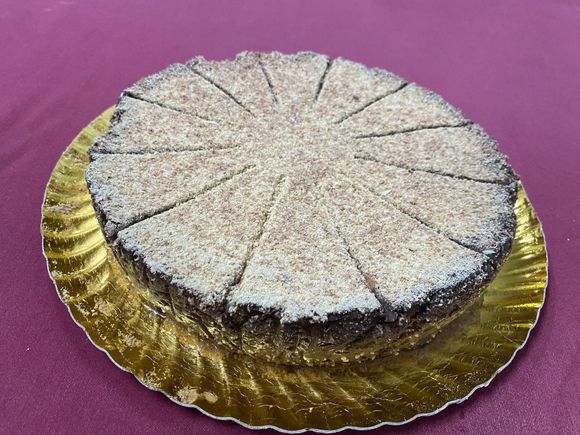Un pastel de chocolate reposa sobre un plato dorado sobre una mesa morada.