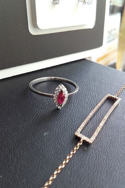 Un anillo con piedras preciosas negras y rojas junto a una pulsera rectangular de oro sobre una superficie texturizada.