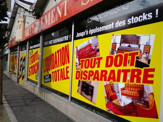 Affiche indiquant une liquidation posée sur une vitrine qui donne dans la rue.