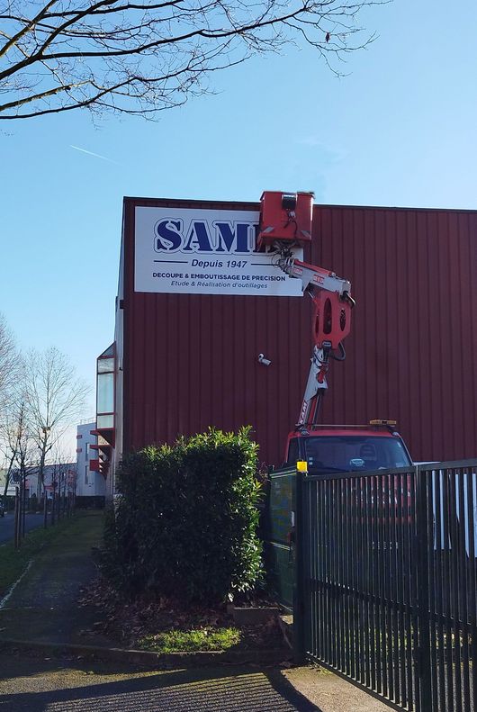 Enseigne en cours de pose sur un bâtiment industriel.