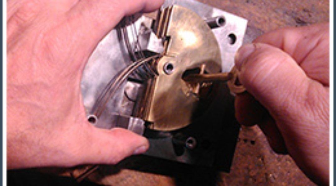 Manos insertando la llave en un mecanismo de cerradura de latón montado sobre una placa de metal.