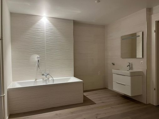 Salle de bain moderne avec baignoire blanche, lavabo et carrelage mural texturé réalisée par Genc Carrelage