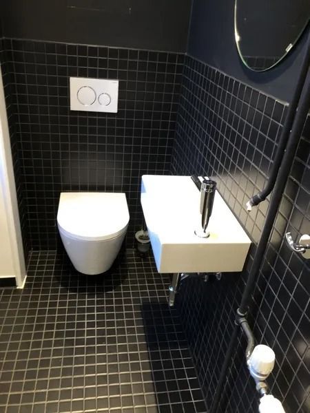 Salle de bain carrelée noire avec WC et lavabo suspendus, murs foncés.