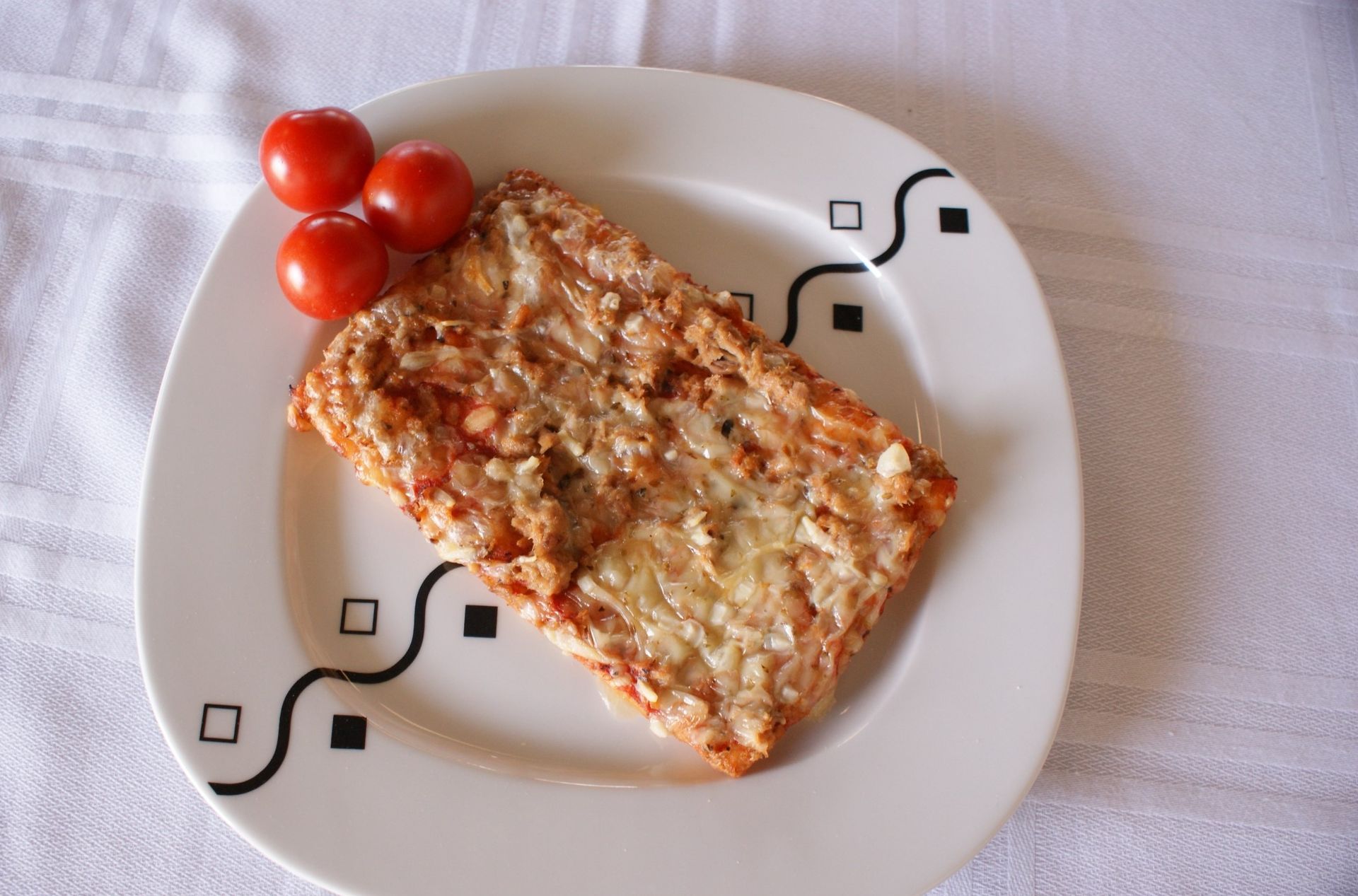 Un plato blanco cubierto con un trozo de pizza y tomates.