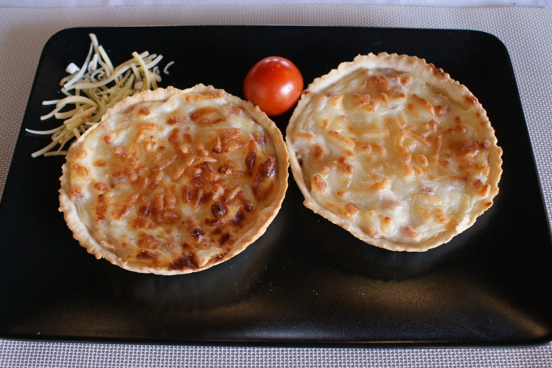 Dos pizzas en un plato negro al lado de un tomate.