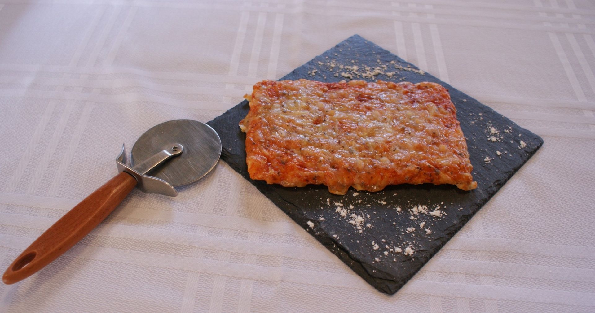 Un trozo de pizza está sobre una tabla de cortar de pizarra al lado de un cortador de pizza.