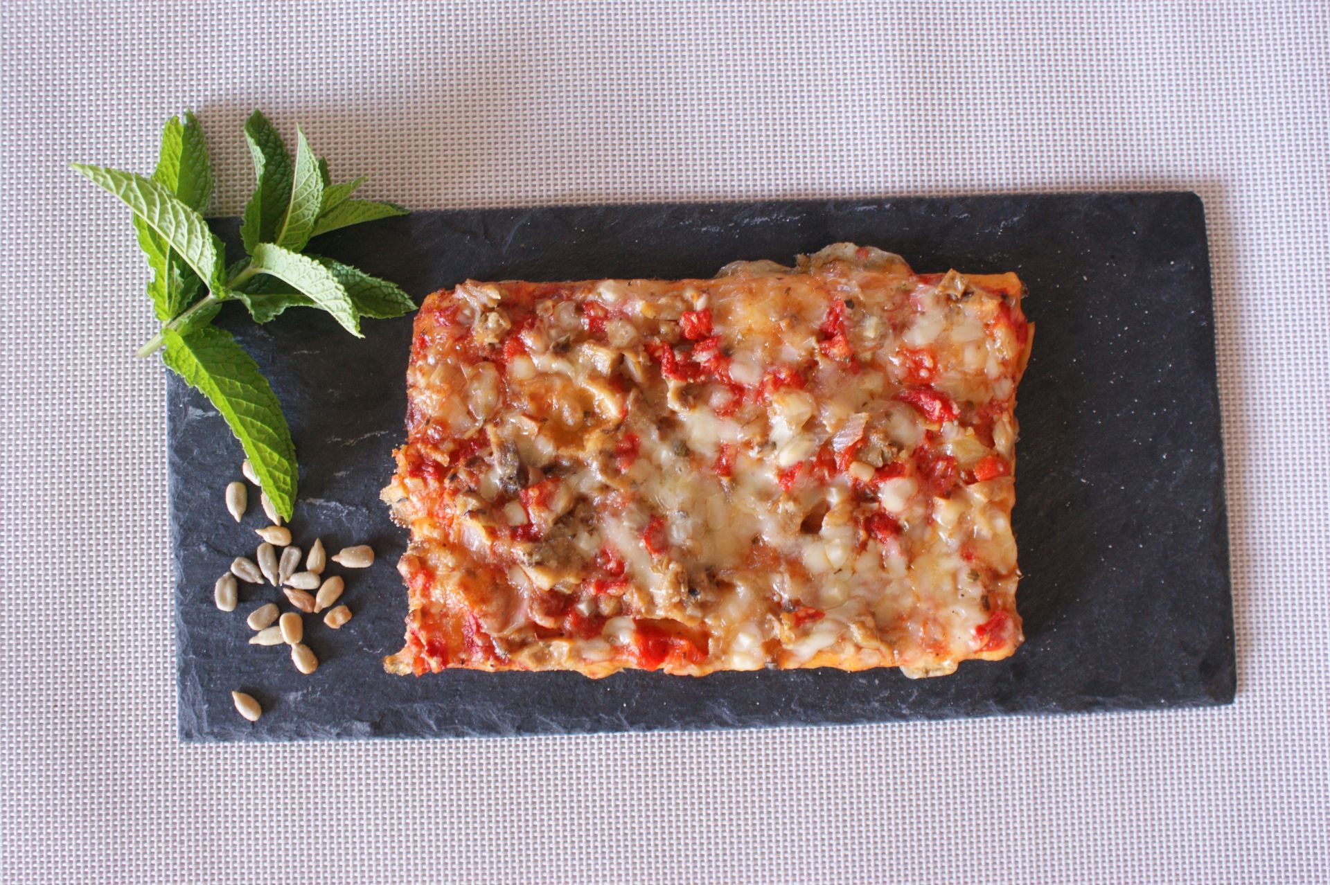 Un trozo de pizza está sobre una tabla de cortar de pizarra sobre una mesa.