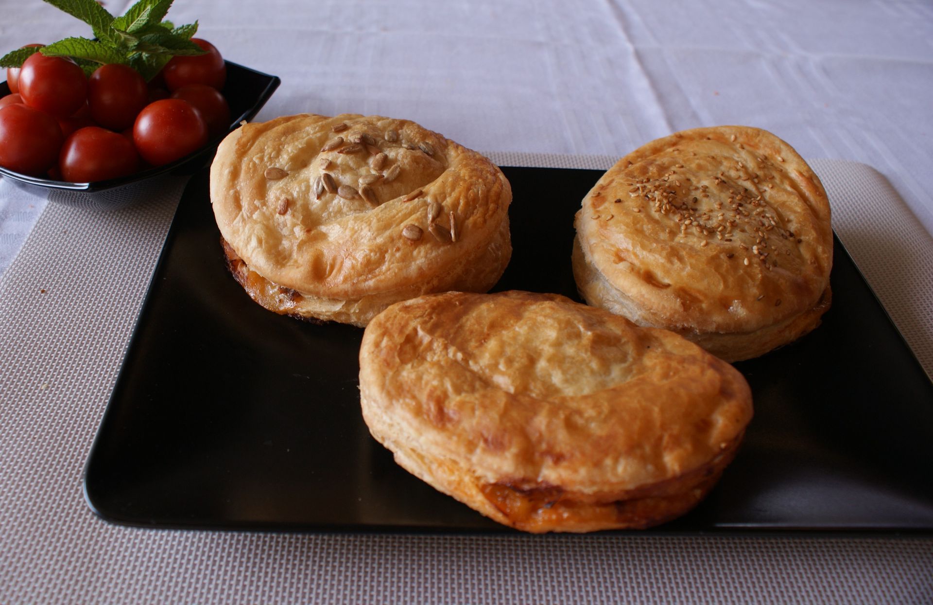 Tres pasteles en un plato negro con un bol de tomates al fondo