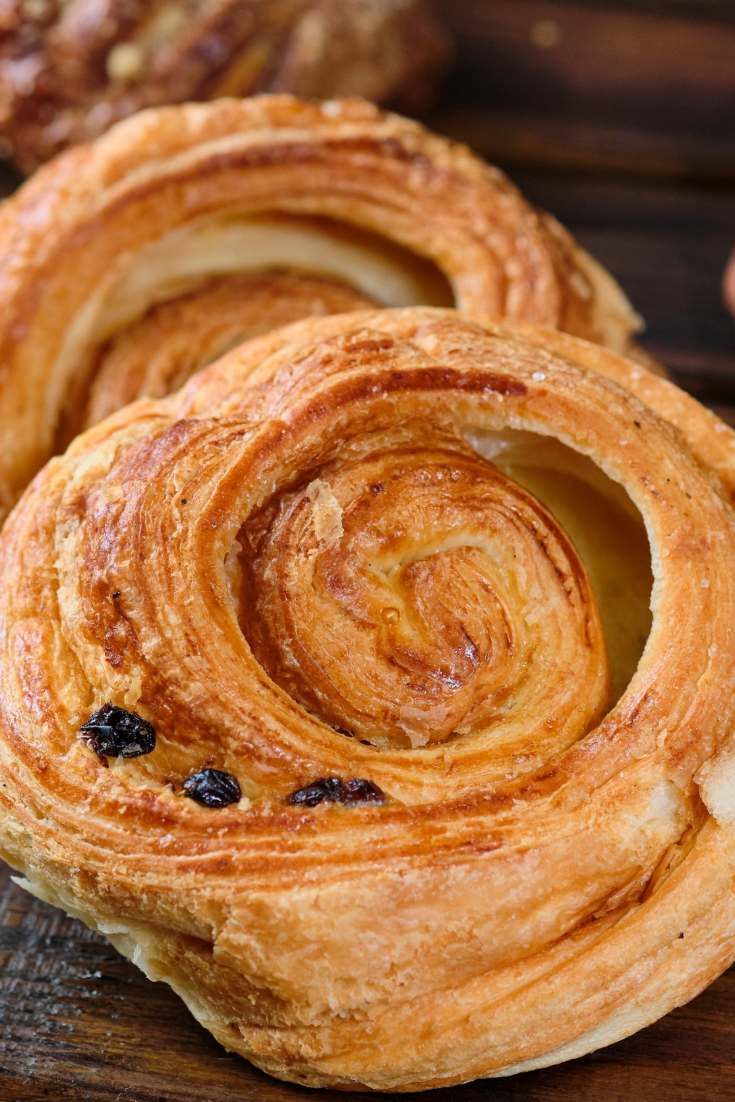 Un primer plano de dos pasteles daneses con pasas en una mesa de madera.