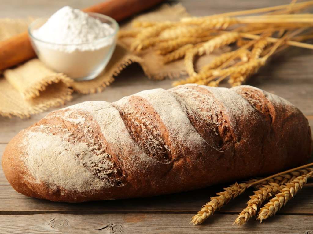 Una hogaza de pan está sobre una mesa de madera al lado de espigas de trigo y harina.