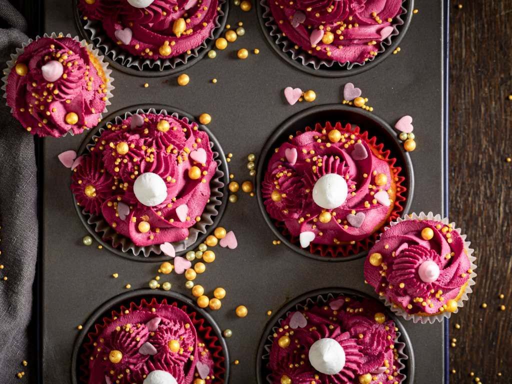 Los cupcakes están decorados con glaseado rosa y chispas doradas.