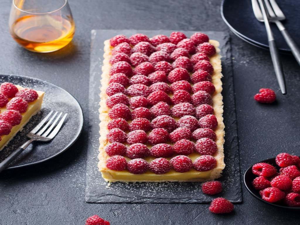 Sobre una mesa hay un pastel con frambuesas encima.