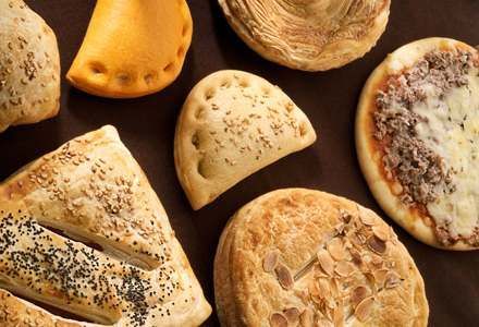 En una mesa hay una variedad de pasteles y pizzas.