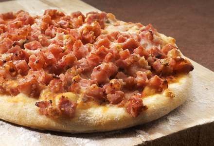 Una pizza con tocino encima está sobre una mesa de madera.