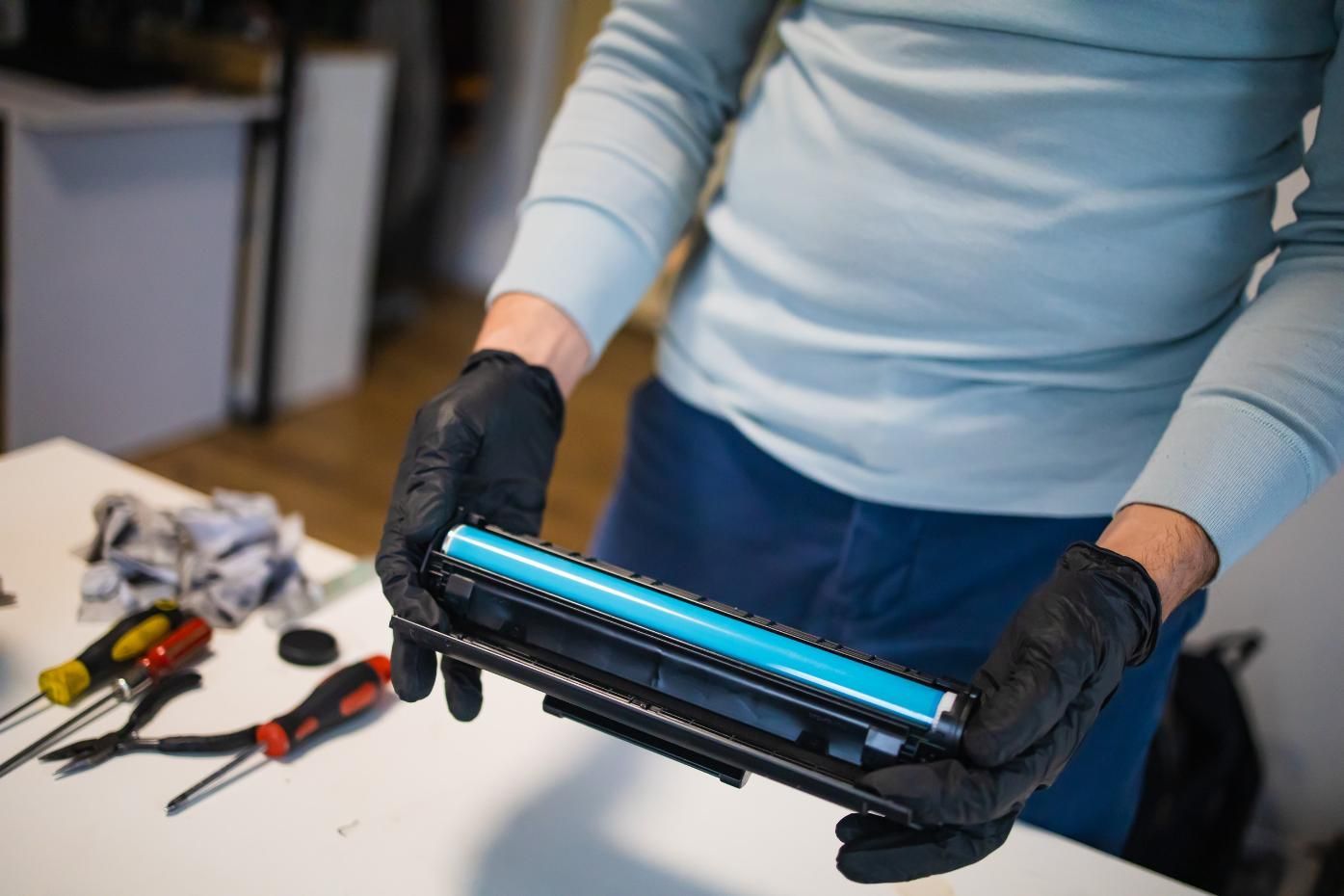 Persona que lleva guantes negros sosteniendo un cartucho de tóner cian.