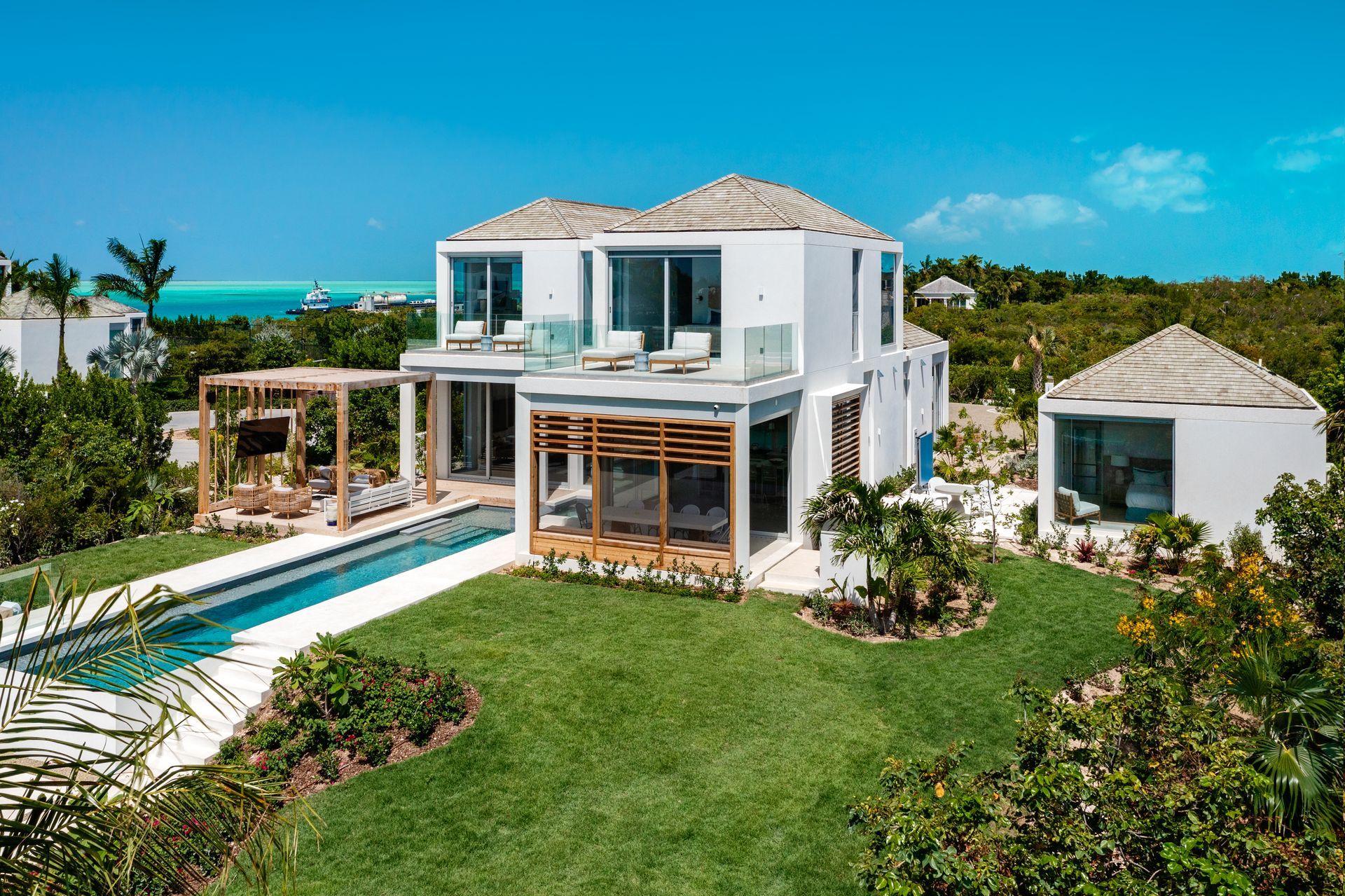 A large white house with a swimming pool in the middle of a lush green field.