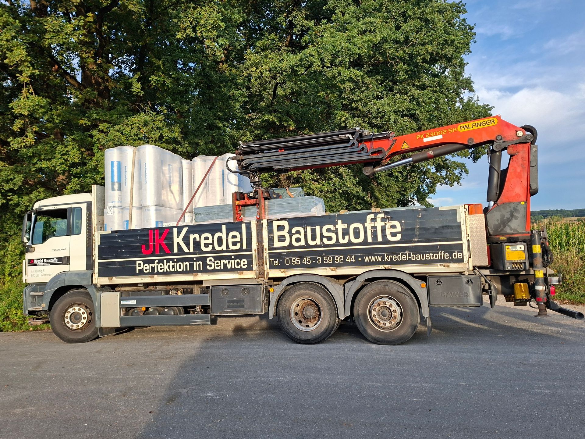 MAN-Lkw der JK Kredel Baustoffe mit Ladekran, seitliche Ansicht auf dem Hof